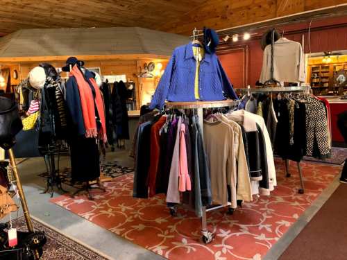 A cozy boutique interior featuring clothing racks with various garments and a patterned rug on the floor.