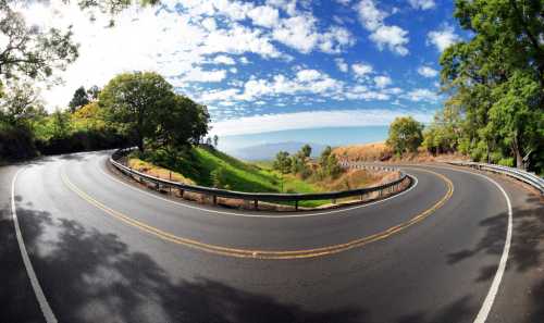 A winding road curves through lush greenery under a bright blue sky with scattered clouds.