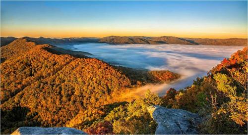 A scenic view of rolling hills covered in autumn foliage, with mist rising over the valley at sunrise.