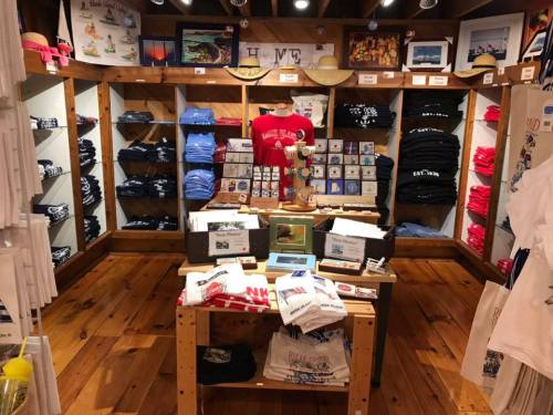 A gift shop interior featuring shelves of colorful t-shirts, postcards, and souvenirs on display.