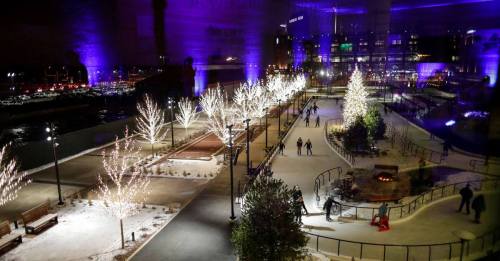A winter scene with illuminated trees, an ice skating rink, and people enjoying the festive atmosphere at night.