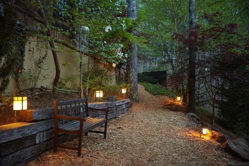 A serene garden path lined with lanterns, featuring a wooden bench and surrounded by lush greenery and trees.