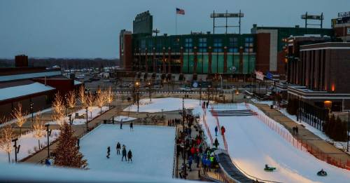 A winter scene featuring an ice rink and sledding hill, with a stadium in the background and people enjoying the snow.