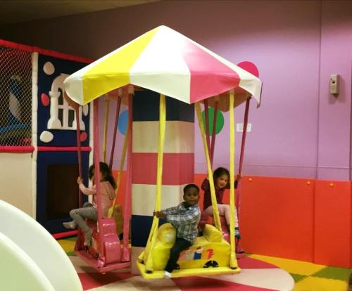 Three children play on a colorful carousel in a vibrant indoor play area.