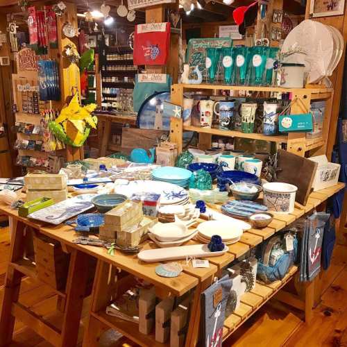 A vibrant display of various decorative items and tableware arranged on wooden tables in a cozy shop.