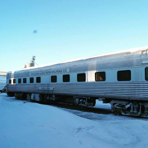 A silver train car labeled "Wisconsin & Southern Railroad Co." parked on snow-covered ground under a clear blue sky.