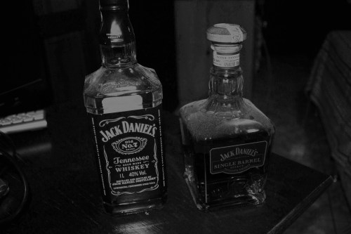 Two bottles of Jack Daniel's whiskey on a dark wooden surface, one labeled "Tennessee Whiskey" and the other "Single Barrel."