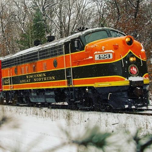 A vintage orange and black train labeled "Wisconsin Great Northern 423" on a snowy track surrounded by trees.