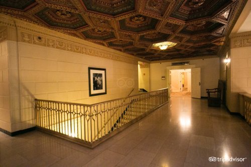 Elegant hallway with ornate ceiling, decorative railing, and a framed picture on the wall. Soft lighting enhances the ambiance.