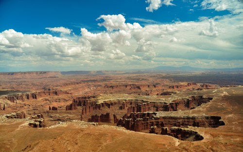 A vast desert landscape with rocky formations under a blue sky filled with clouds.