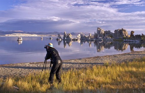 A photographer captures the serene landscape of a lake with unique rock formations and a colorful sky.