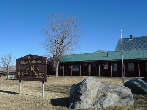 Sign for the Milton Gotchard Museum & Park in front of a building with a green roof and a clear blue sky.