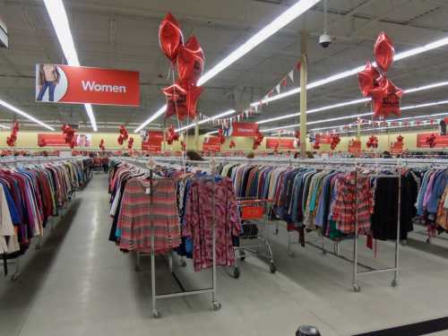 A clothing store aisle for women, featuring racks of colorful clothes and red balloons overhead.