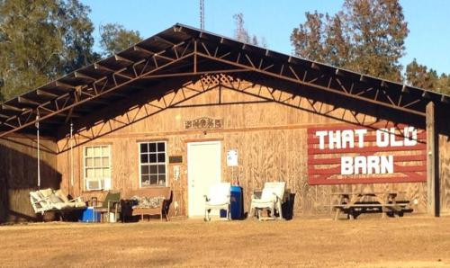 A rustic barn with a sign reading "That Old Barn," surrounded by chairs and a table on a grassy area.