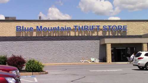 Exterior of Blue Mountain Thrift Store, featuring a large sign and parked cars in front.