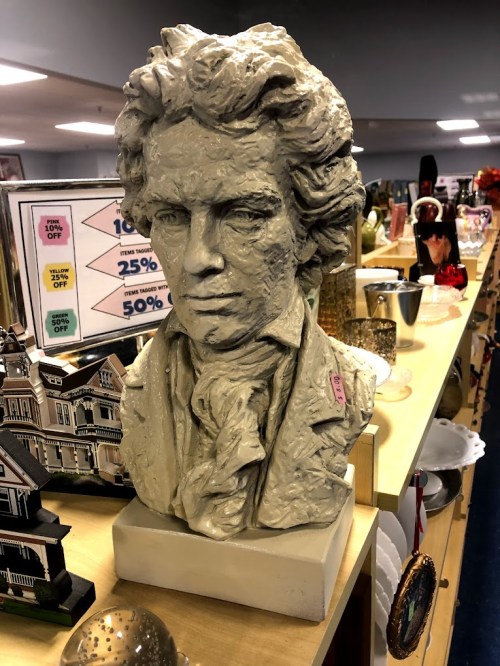 A sculpted bust of a man with curly hair, displayed on a shelf among various decorative items.