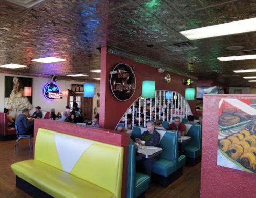 A colorful diner interior with retro decor, featuring booths, neon signs, and patrons enjoying their meals.