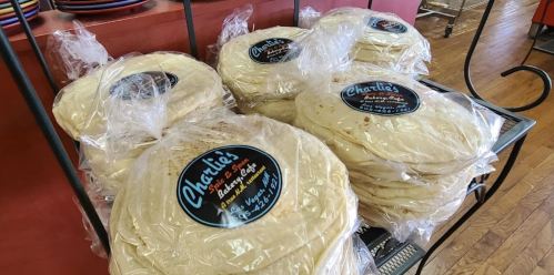 A display of packaged flatbreads labeled "Charlie's Bakery & Cafe" stacked on a shelf in a cozy setting.