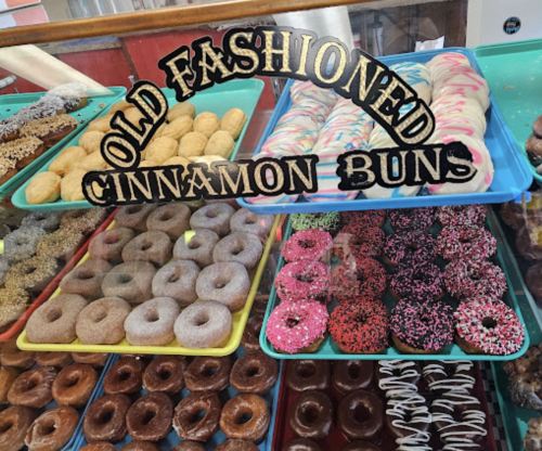 A display of various donuts and cinnamon buns in colorful trays, with a sign reading "Old Fashioned Cinnamon Buns."