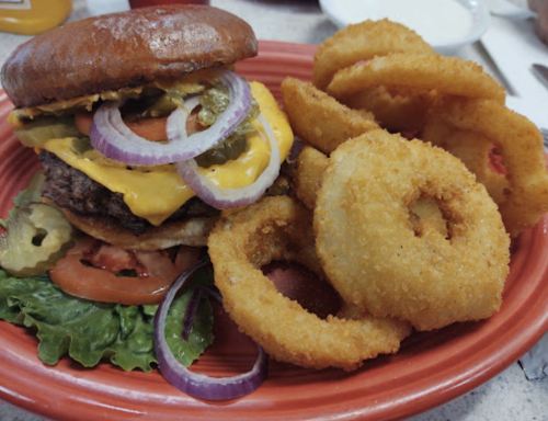 A juicy cheeseburger with lettuce, tomato, pickles, and onions, served with crispy onion rings on a red plate.