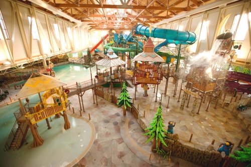 Indoor water park featuring slides, play structures, and a tropical theme with trees and water features.