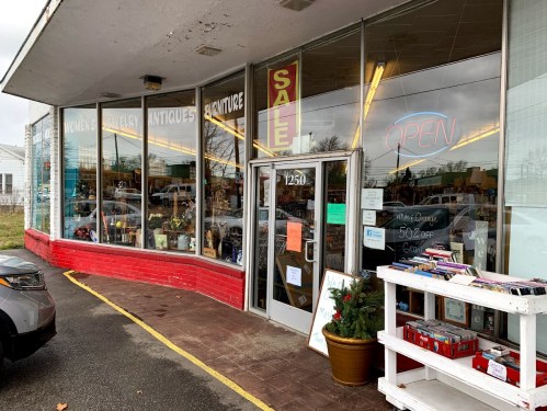 A vintage store with large windows displaying antiques and a bright "OPEN" sign, featuring a sale announcement.
