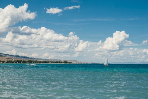 A serene seascape with a sailboat on calm waters under a blue sky filled with fluffy white clouds.