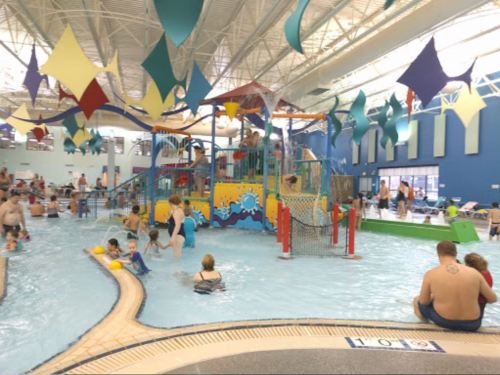 A vibrant indoor water park with colorful decorations, children playing in the water, and adults relaxing nearby.