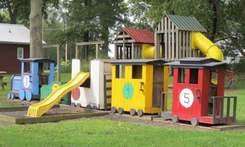 Colorful train-themed playground structure with slides and playhouses in a grassy area.