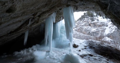 Icicles hang from a rocky cave entrance, with a snowy landscape visible in the background.