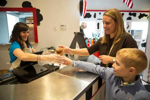 A woman and a boy receive ice cream from a smiling server at a colorful ice cream shop.