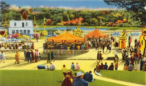 A vibrant carnival scene with colorful tents, crowds of people, and vintage cars near a lake surrounded by trees.