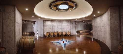 A spacious wine cellar with wooden barrels, a star design on the floor, and modern lighting.