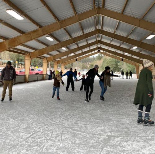 A group of people ice skating indoors under a large, open structure with a metal roof.