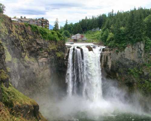 A stunning waterfall cascades down rocky cliffs, surrounded by lush greenery and a distant lodge in the background.