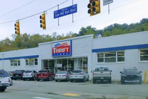 A thrift store with a large sign, surrounded by parked cars and traffic lights on a busy street.