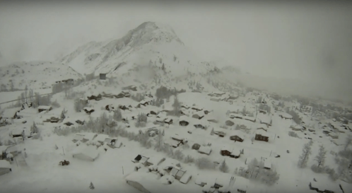 Aerial view of a snow-covered village surrounded by mountains in a winter landscape.