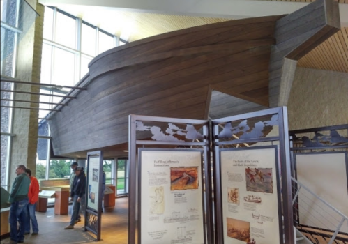 A wooden boat structure inside a museum, with informational displays and visitors in the background.