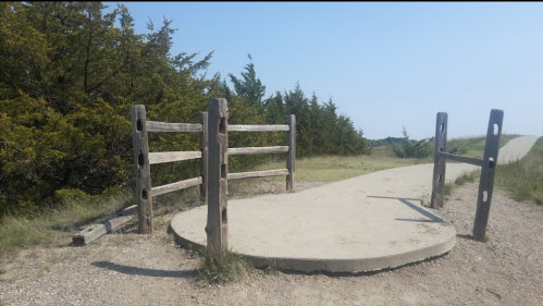 A circular concrete platform with wooden railings, surrounded by grass and trees, near a walking path.