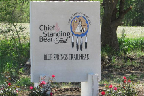 Sign for Chief Standing Bear Trail at Blue Springs Trailhead, featuring the Ponca Tribe of Nebraska logo and flowers.