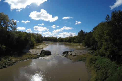 A serene river scene with blue skies, fluffy clouds, and lush greenery along the banks.