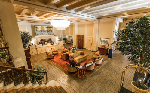 Elegant hotel lobby with plush seating, a chandelier, and decorative plants, featuring a warm, inviting atmosphere.