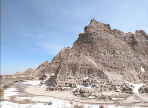 A rugged landscape featuring towering rock formations and a clear blue sky, with patches of snow on the ground.