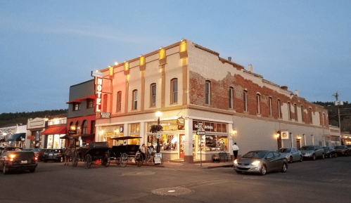 Historic hotel building at dusk, with vintage signage and nearby shops, surrounded by parked cars.