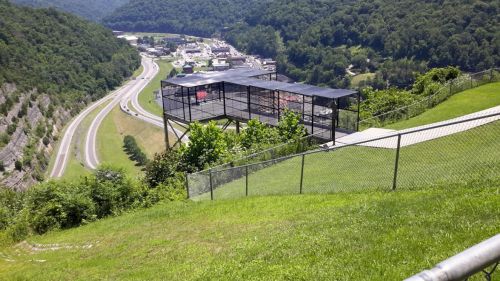 A view of a green hillside overlooking a highway and a large, covered structure in the distance.