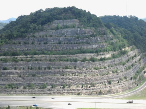 A terraced hillside with greenery, overlooking a highway below, surrounded by rolling hills in the background.