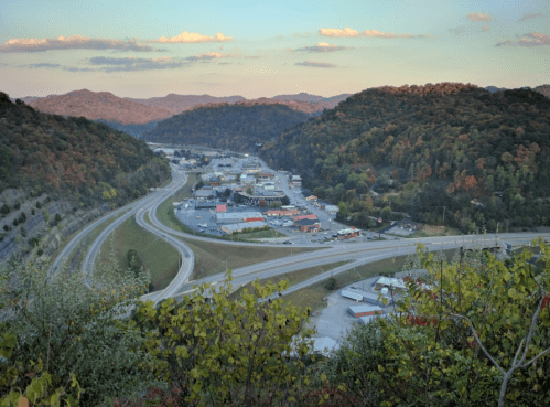 A scenic view of a winding highway surrounded by hills and autumn foliage, with a small town in the valley below.