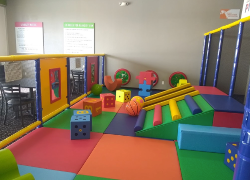 Colorful indoor play area with soft mats, climbing structures, and various toys for children.
