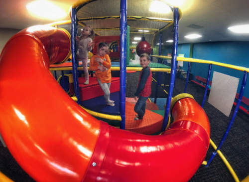 Children playing in a colorful indoor playground with slides and climbing structures.
