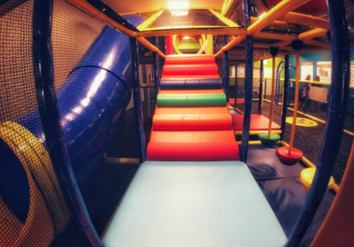 Colorful indoor playground with slides, climbing structures, and soft play areas. Brightly lit and inviting for children.